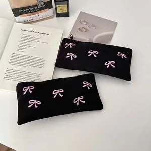 Black cotton pencil case with pink bow embroidery on a lifestyle aesthetic background