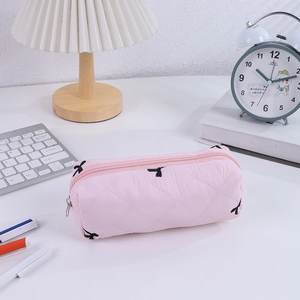 Pink quilted pencil case with bow embroidery shown on a desk with stationery and lamp
