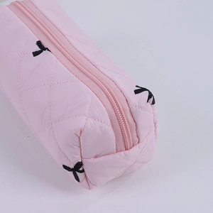 Close-up of pink quilted pencil case with black embroidered bows and silky texture