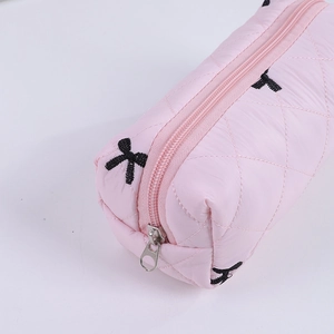 Detailed macro shot of pink quilted fabric texture with black embroidered bow and metal zipper