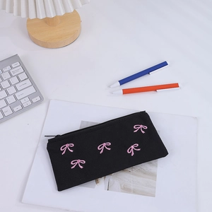 Dettaglio dell'astuccio in tela nera con fiocchi rosa ricamati e chiusura a zip sicura