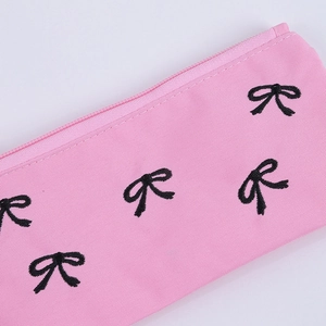Dettaglio ravvicinato dell'astuccio in tessuto rosa con fiocchi neri e zip liscia