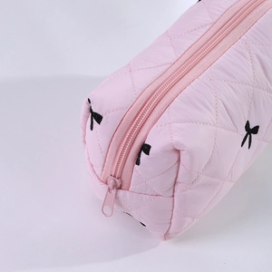Détail de la trousse matelassée rose avec motifs de nœuds noirs et fermeture éclair