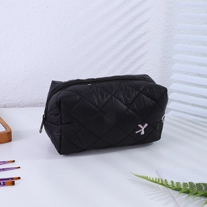 Détail d'une trousse de maquillage matelassée noire avec nœud rose à paillettes et zip