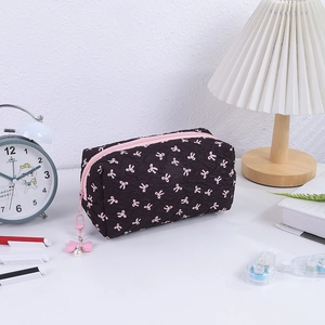 Detailed view of black quilted makeup bag with pink bow print and pearl pendant