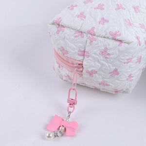 Close-up of cute pink bow pendant with pearls on a quilted white makeup bag