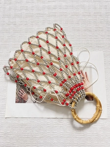 Handmade woven pearl net tote bag with red beads and bamboo handle on white fabric