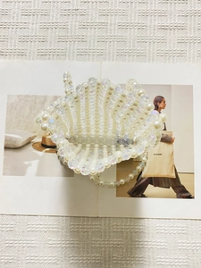 Elegant pearl beaded mini crossbody bag with woven shell shape on a fashion magazine