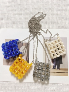 Detail of four colorful beaded crossbody bags with metal chains on textured white fabric