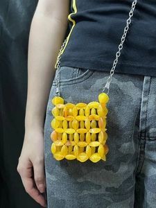 Macro detail of hand-woven yellow beaded mini crossbody bag with silver metal chain