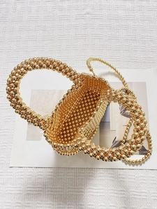 Sac cabas doré à perles tissées avec poignée et bandoulière sur fond minimaliste
