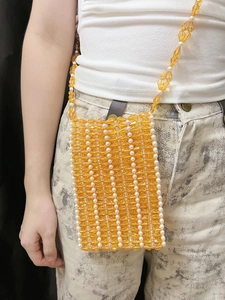 Détail du sac de téléphone en perles acryliques ambre et blanc porté par un mannequin