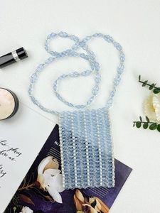 Vue à plat d'un sac de téléphone en perles bleu clair fait main sur un fond en tissu blanc