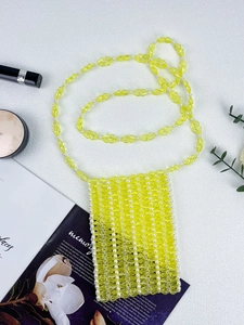 Vue à plat d'un sac à bandoulière en perles jaunes fait main avec perles sur fond blanc texturé