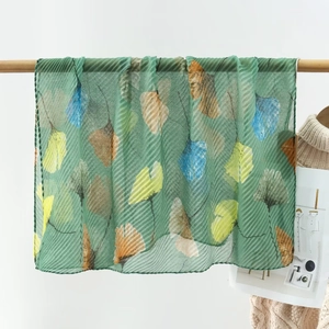 Detail of emerald green pleated scarf with colorful ginkgo leaf print and airy texture