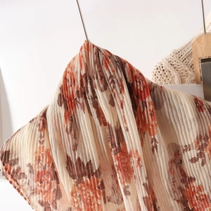 Close-up of pleated floral scarf in orange and brown tones on a wooden hanger