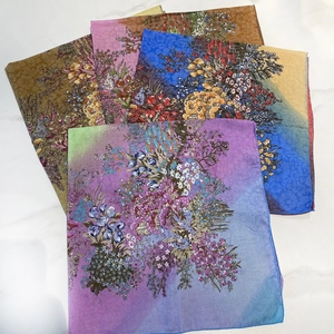 Gros plan de cinq foulards carrés colorés à motif floral sur un fond de marbre blanc