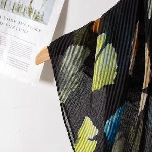 Detail of pleated summer scarf featuring artistic ginkgo leaf prints on black fabric