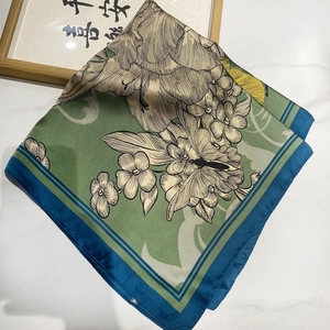 Detail of silk square scarf featuring green floral patterns and dark teal borders