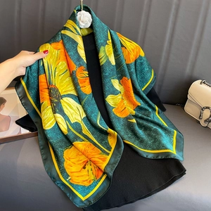 Luxurious dark green silk scarf with vibrant yellow floral print draped on a hanger