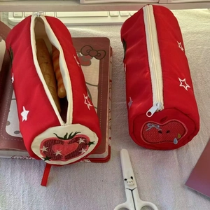 Detail of red cylinder pencil cases with embroidered stars and cute fruit motifs
