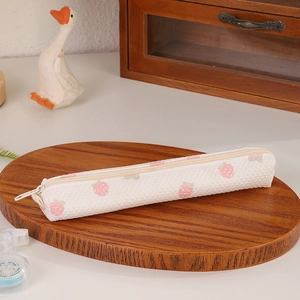 Close-up of strawberry print pencil case with honeycomb texture on a wooden tray