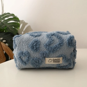 Macro view of plush light blue makeup bag with embroidered dark blue hearts and woven label