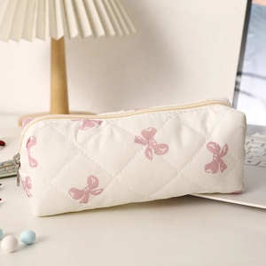 Détail de la trousse matelassée blanche avec imprimé nœuds roses sur un bureau blanc