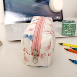 Détail d'une trousse matelassée avec nœuds roses et fermeture éclair métallique lisse