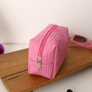 Detail of pink quilted makeup bag showing woven texture and metal zipper closure