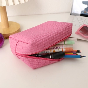 Detailed view of pink woven makeup bag filled with pens and lipstick on a desk