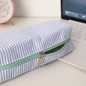 Detail of blue striped seersucker pencil case with light green zipper on white desk