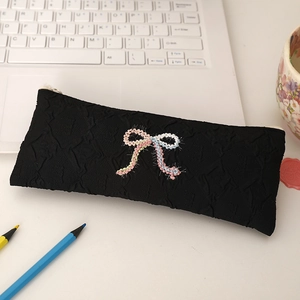 Macro detail of black bubble fabric pouch with colorful crochet bows and white zipper