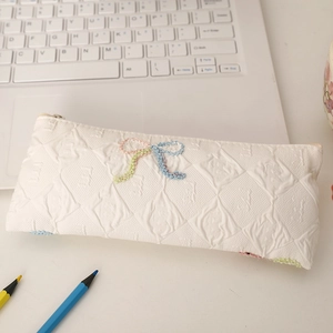 Detail of white jacquard pencil case with textured rhombus pattern and colorful woven bow