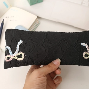 Detail of black pleated fabric pencil case with colorful woven ribbon and zipper closure