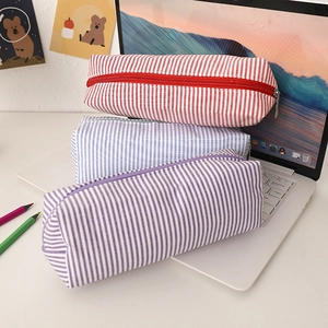 Three seersucker pencil cases with striped patterns stacked on a white laptop keyboard