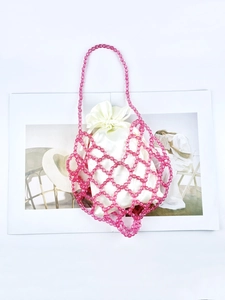 Pink beaded woven shoulder bag with white satin drawstring liner on a magazine background