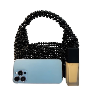 Detail of a black beaded Boston handbag with a phone and perfume for scale