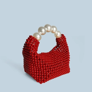 Détail d'un sac à perles rouges avec de grandes poignées en perles blanches sur fond bleu