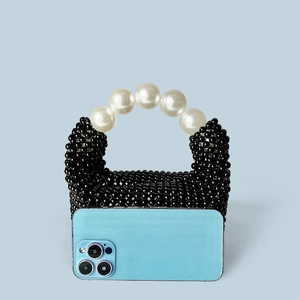 Mini sac à main perlé noir avec poignée en perles blanches à côté d'un smartphone