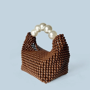 Détail du sac tressé marron foncé avec poignée en grandes perles blanches sur bleu