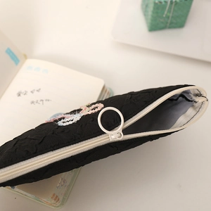 Close-up of black quilted pencil case with colorful embroidery and round zipper puller