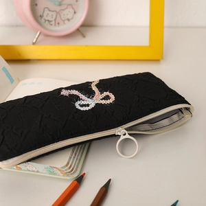 Detail of black quilted pencil case with bow embroidery and a white circular zip pull