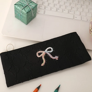 Detail of black puffy bubble fabric pencil case featuring a colorful woven bow accent