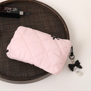 Pink quilted makeup bag with black bow charm and pearl detail on a woven tray