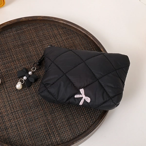 Detailed shot of a black quilted makeup bag featuring pink bow embroidery and pearl charm