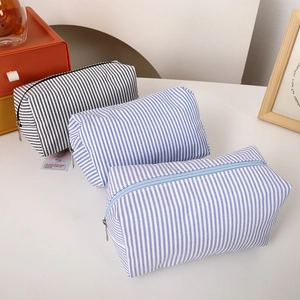 Detailed view of three striped canvas cosmetic bags with top zippers on a white table
