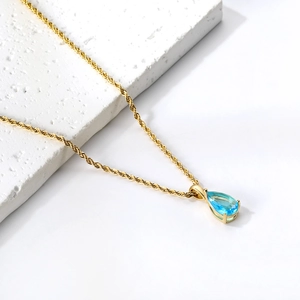 Détail d'un pendentif avec pierre bleu clair taille poire et sertissage doré à 4 griffes