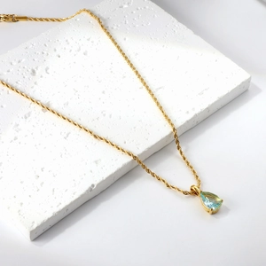 Détail d'un pendentif goutte d'eau bleue claire sur une chaîne torsadée plaquée or 18K
