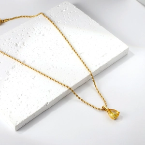 Détail d'un collier en chaîne torsadée dorée avec pendentif en pierre jaune poire